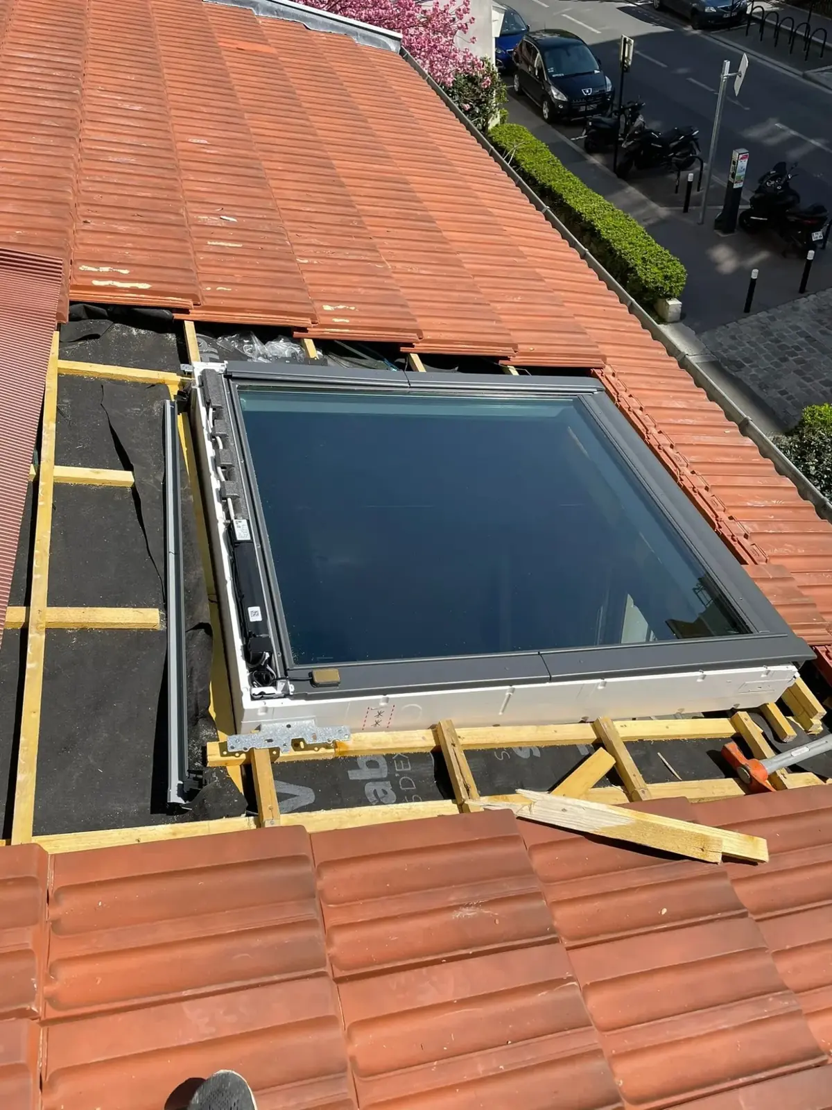 Fenêtre de toit en cours de pose dans une toiture en tuiles, cadre et chevêtre visibles