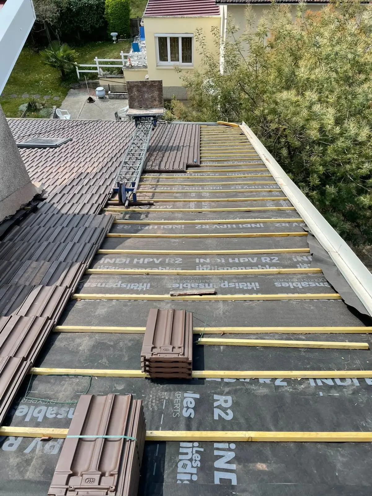 Réfection de toiture en cours : liteaux neufs et tuiles brunes en attente